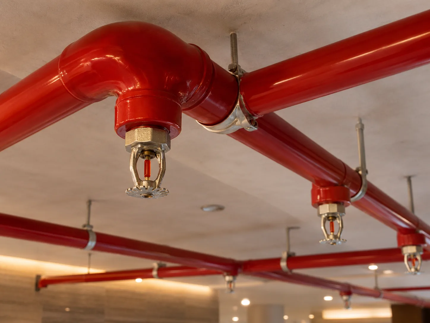 Red fire fighting pipes and sprinkler heads running across a concrete ceiling